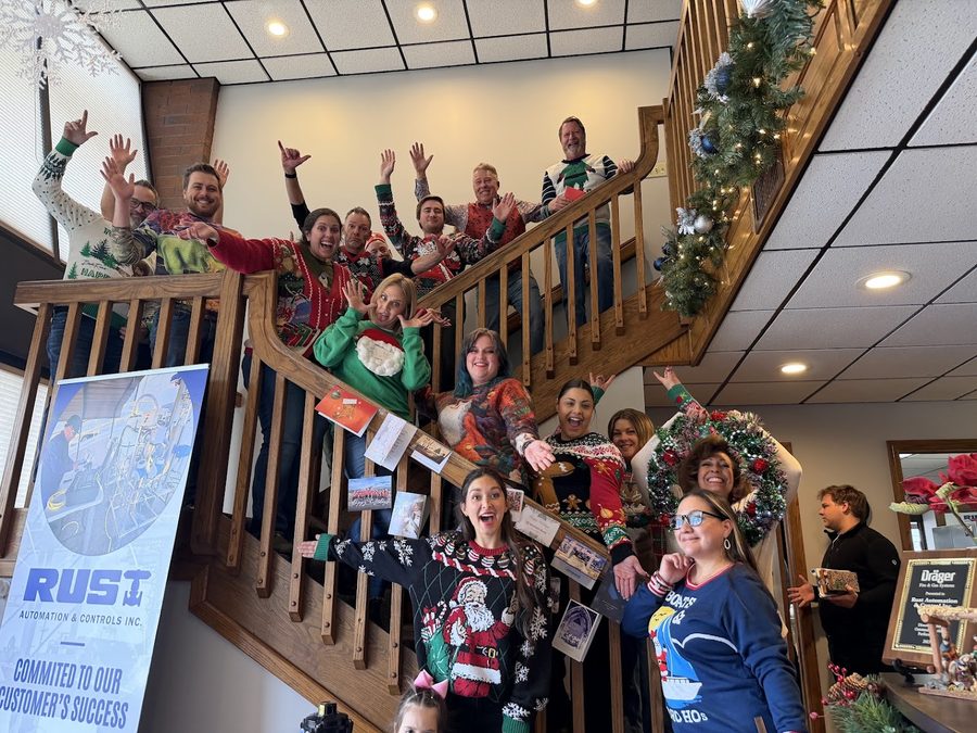 Rust employees on a staircase in the office, waving, with holiday decorations and a Rust banner behind them