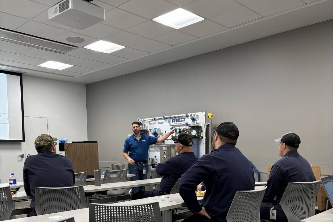 An instructor demonstrating a Rust-branded industrial training unit to five trainees in a classroom