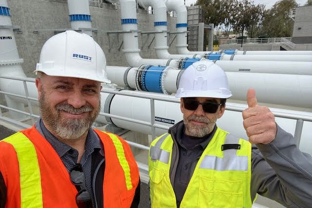 Two members of the Rust team in hard hats and high-visibility vests in front of large-diameter pipework and valves at a treatment plant